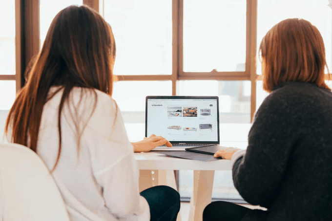 two women at desk looking at laptop