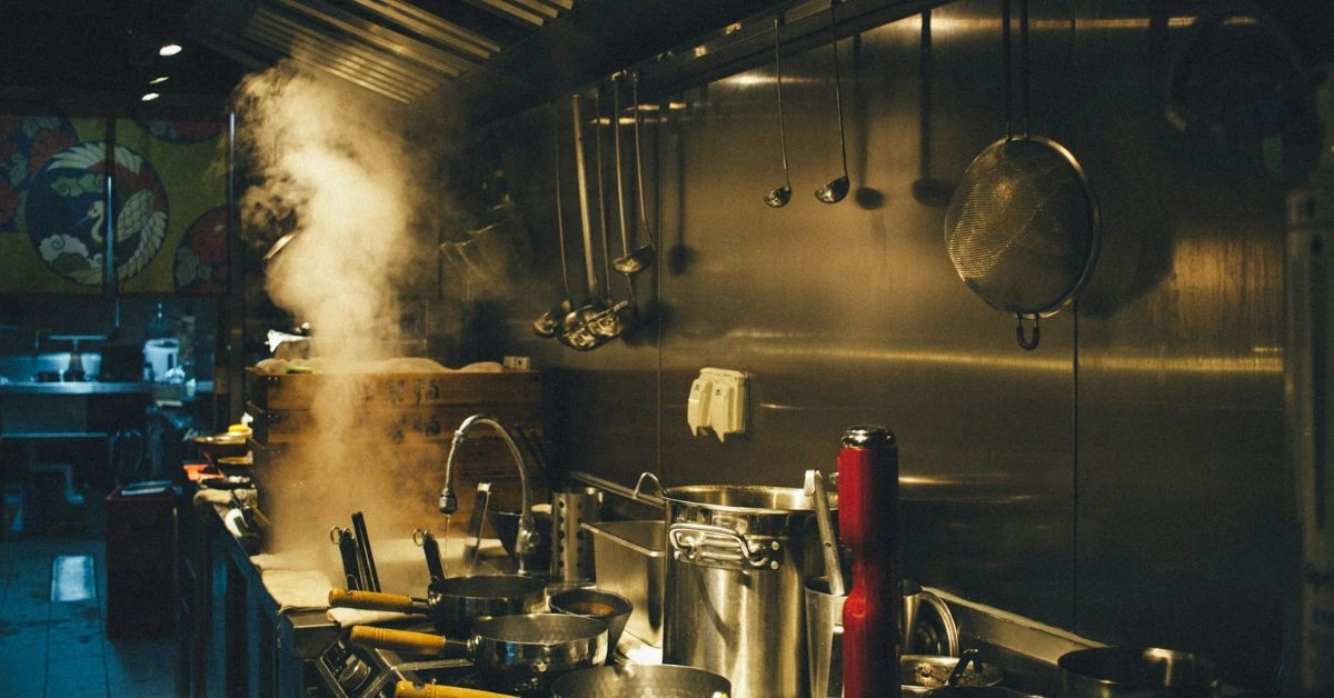 Steamy commercial kitchen in Nashville with hanging ladles, large pots, and busy cooking equipment.